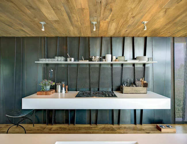 A black perforated-metal screen behind the kitchen's floating cooktop conceals downdraft vents.