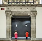 Beyond an existing stone archway, a black solid surface&ndash;clad wall with simple icons directs visitors to the renovated Currelly Gallery washrooms.