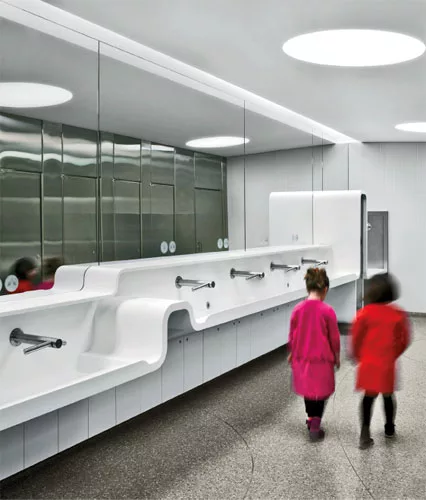 Undulating sink troughs composed of white solid surfacing are striking new additions to the updated washrooms at the Royal Ontario Museum. In the women’s room, the surfacing also wraps a diaper 