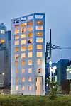 Reflecting light into the interior, silver paint coats the building’s exterior. Devoid of scale-defining sashes, the windows read as wall openings that widen as the building ascends. The double-