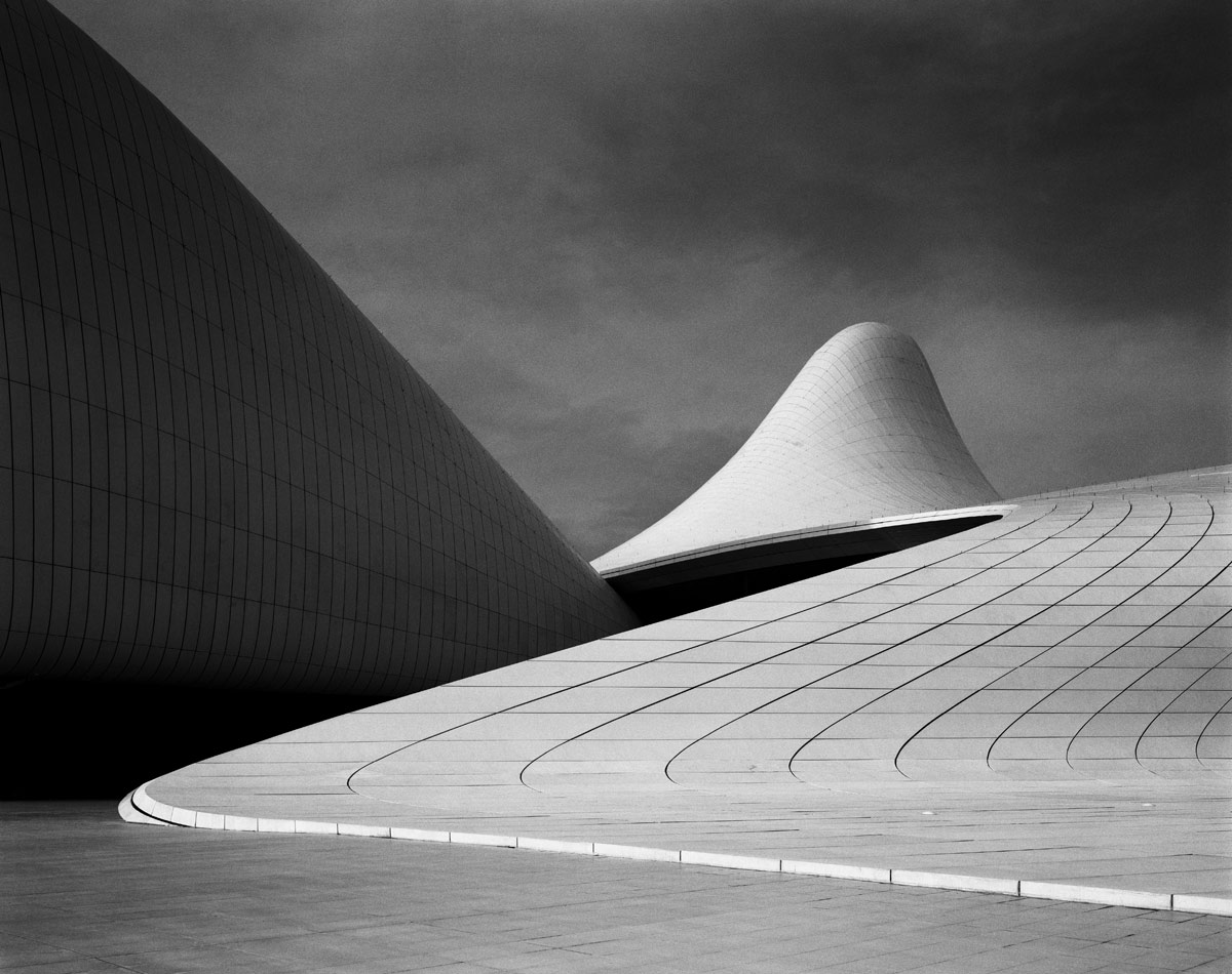 <br><h9>Heydar Aliyev Centre by Zaha Hadid Architects <br>Baku, Azerbaijian, photo © Hélène Binet, courtesy Ammann Gallery, 2013</h9><p>   </p><h6><strong>HÉLÈNE BINET</strong><br>
Photographer based in London<p>   </p>I have been working for 30 years to capture architectural space
in photographs. I spend about half my time in the commercial
world and half my time doing personal work. Recently I’ve been
photographing traditional Korean architecture, which is astonishing.
The photos may become a book.<p>   </p>
There are a few architects I’ve been working with for many
years, including Peter Zumthor and Caruso St John. I like to have
long relationships—I feel I grow with the architects; it’s not just
shooting and going home. Zaha Hadid was very important to my
career. I shot all of her buildings starting with Vitra. There was
something primordial about her work, something very deep,
which I hope I brought out in my photos. She’s often been misunderstood.
Some people see her work as fashionable; I was never
interested in that.<p>   </p>
I shoot mostly in black-and-white. The way we experience
space is a complex thing, and color can compete with that experience.
I go in the other direction. I prefer silence. I shoot on film; I
don’t touch digital. I use a 4x5 camera called an Arca-Swiss—you
put a film plate in and put a blanket over your head. It’s expensive,
and it’s slow. Each image is a commitment. It’s like a
performance: you have to be very good in the moment; you don’t
get a chance to fix it later. I might make 20 images in a day, eight
or nine that I’m happy with. I do all the printing myself, choosing
everything: the paper, the contrast. The actual print is very
important to me. A reproduction of the work is not the work.