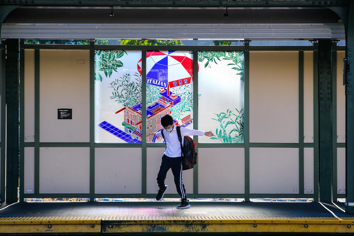 a young boy on ane elevated subway platform in front of colorful stained glass.